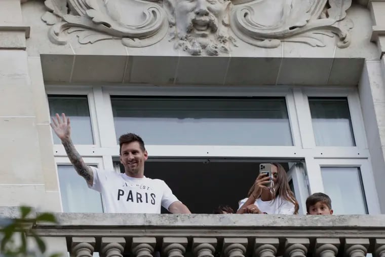Lionel Messi (left) waves to fans from the balcony of his hotel room in Paris, watched by his wife Antonella Roccuzzo (center) and one of their children.