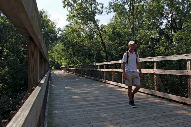 A man in Wissahickon Valley Park walks along a former railroad trestle that's now a pedestrian bridge.