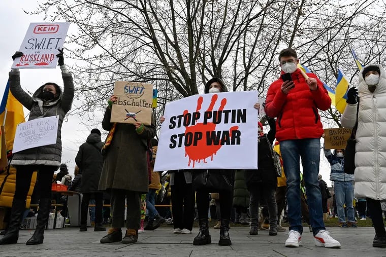 Demonstrators hold placards reading, from left, "No SWIFT for Russia," "Turn off SWIFT", "Stop Putin, Stop War" during a protest against Russia's invasion of Ukraine in front of the Chancellery in Berlin on Friday.