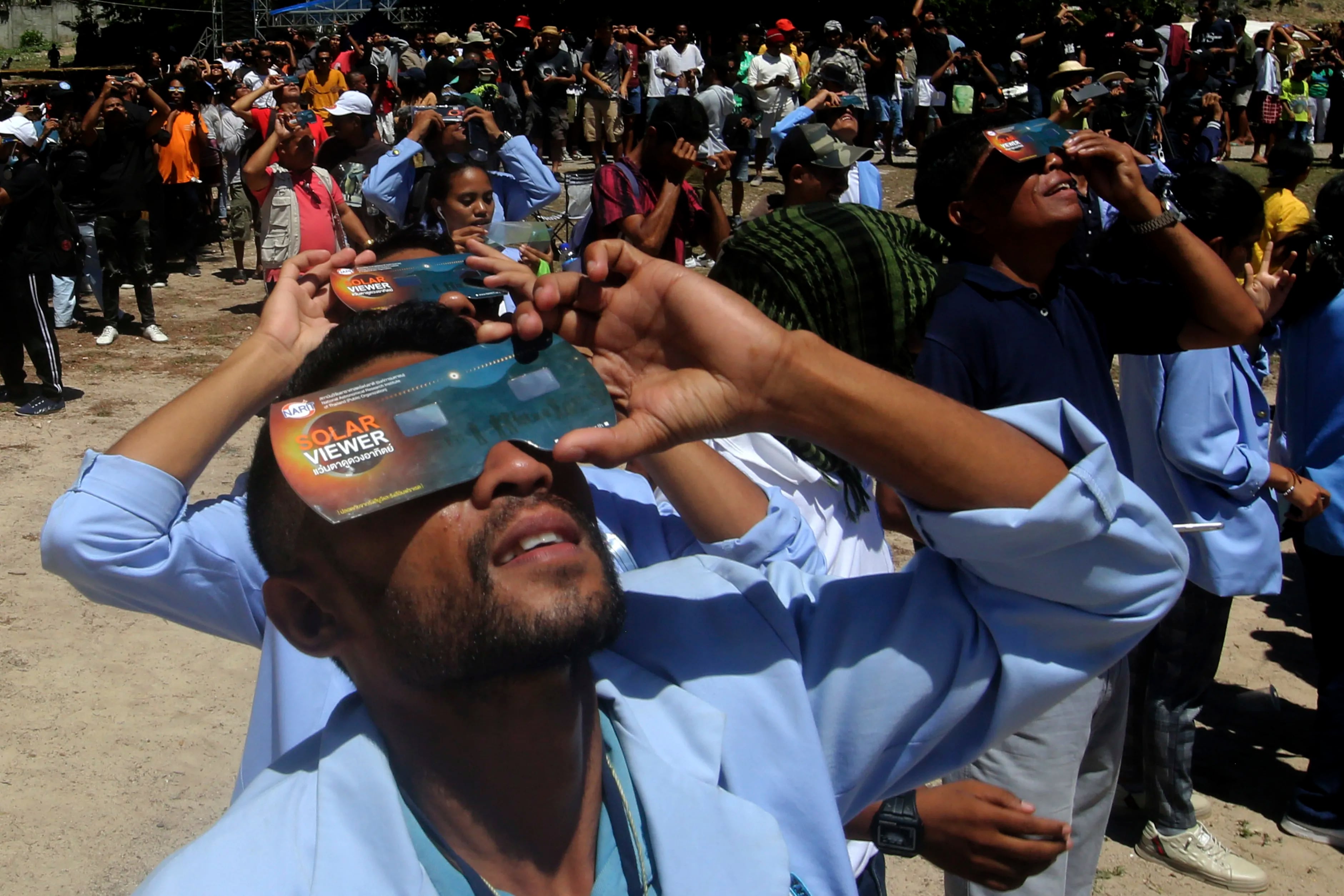 People use protective glasses to watch a hybrid solar eclipse in Lautem, East Timor, on April 20, 2023. The lucky few people in its path either saw the darkness of a total eclipse or a “ring of fire” as the sun peeked from behind the new moon.