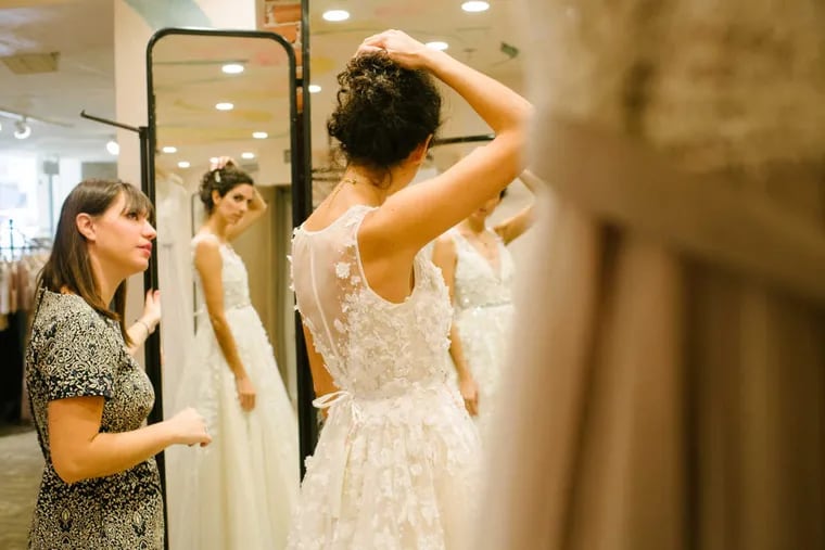 Stylist Beth Rosella helps Ignacia Behncke, 32, try on a wedding dress in BHLDN (pronounced beholden) inside the Anthropologie store in Center City in Philadelphia on Friday, November 18, 2016. BHLDN is the bridal brand for Philly-based Urban Outfitters, Inc., and opened a shop-in-a-shop today. .(Michelle Gustafson/For the Inquirer)