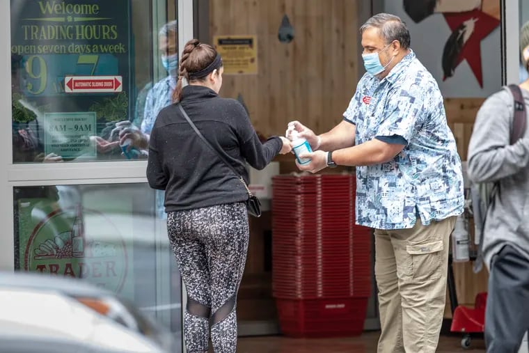 A grocery shopper gets a squirt of hand sanitizer from a masked Trader Joes employee, right, before she is allowed to enter the store on Arch Street in Center City, on Sunday morning April 5, 2020.