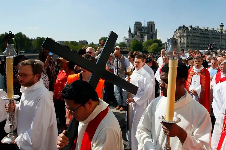 With Notre Dame cathedral in background, religious officials carry the cross during the Good Friday procession, Friday, April 19, 2019 in Paris. Top French art conservation officials say the works inside Notre Dame suffered no major damage in the fire that devastated the cathedral, and the pieces have been removed from the building for their protection.