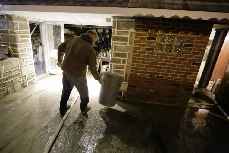 Ed Volmer moves a trash can as water still runs into his basement and garage hours after a large water main burst flooding part of his home on Millbrook Rd. in Phila., PA on January 5, 2017 ELIZABETH ROBERTSON / Staff Photographer ​