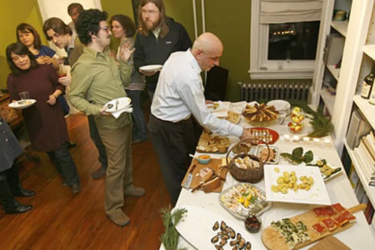 Guests help themselves to the seven-fishes spread at writer Ludwig’s home. Offering platters of hot and cold small bites served cocktail-party style made the feast manageable. (CHARLES FOX / Staff Photographer)