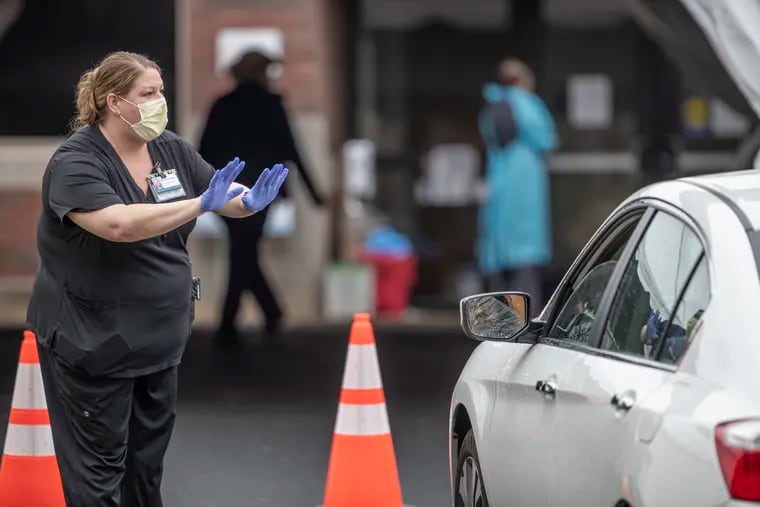 Un trabajador de salud del Hospital Abington-Jefferson le pide a una persona que conduce un vehículo que detenga su automóvil y espere para asegurarse de que tenga una cita para hacerse una prueba de detección de coronavirus, el 17 de marzo de 2020.