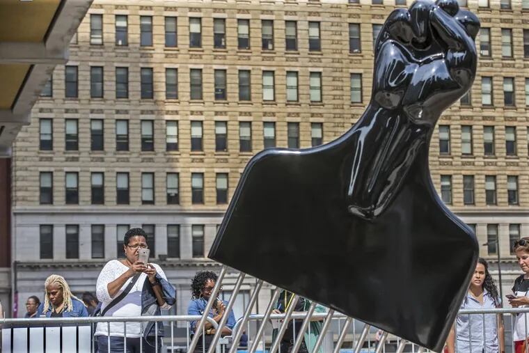 Tia Kelly takes a photograph of the new peice of art on the Thomas Paine Plaza, a large Afro Pick with a Black Powere symbol as they handle on Tuesday September 12, 2017. On Tuesday at 1:30 The Mural Arts Project will add its own touch to the Rizzo statue saga with the installation a 12-foot high Afro Pick near the Rizzo statue. The Pop Art object inspired by Claes Oldenburg's Clothespin has a Black Power Fist as its handle. The temporary installation by artist Hank Willis Thomas is the first salvo of Monument Lab a public art project kicking off Wednesday. Tuesday September 12, 2017 MICHAEL BRYANT / Staff Photographer