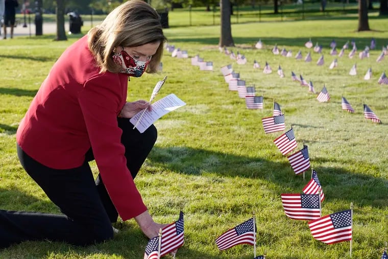 House Speaker Nancy Pelosi kneels to look at small flags placed on the grounds of the National Mall by activists from the COVID Memorial Project to mark the deaths of 200,000 lives lost in the U.S. to COVID-19, Tuesday, Sept. 22, 2020 in Washington. (AP Photo/J. Scott Applewhite)