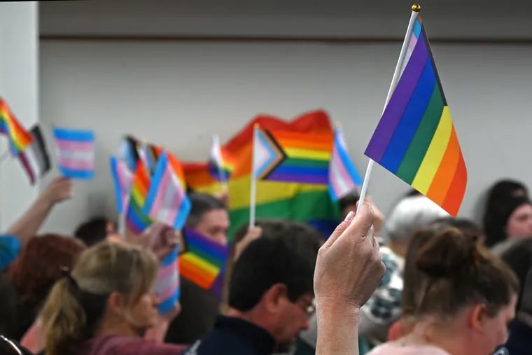 Attendees at a May meeting of the Central Bucks School District wave Pride flags. The district has banned the flags in schools and suspended a teacher who offered support to a transgender student, among other things.