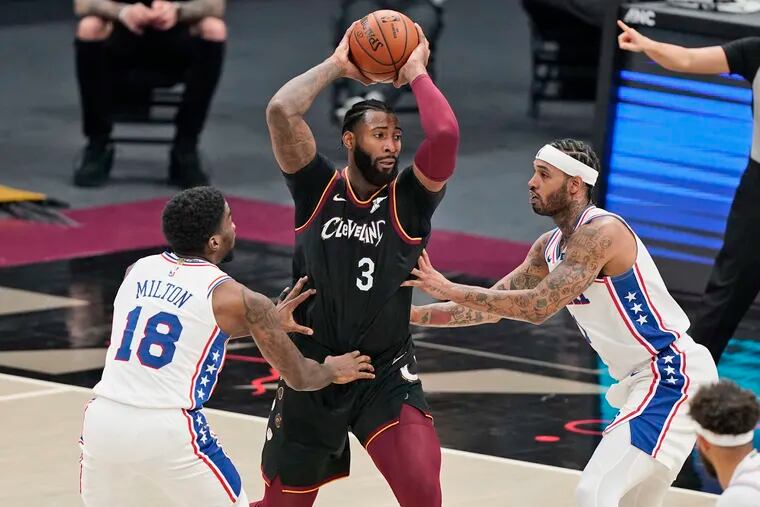 The Cavaliers' Andre Drummond (3) looks to drive between 76ers Shake Milton and Mike Scott.