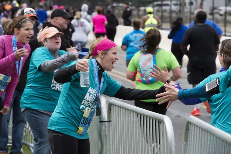 From front to back: runner Amy Fream, 38, from Reading, PA; Amy Wolter, 38, from Temple, PA; and runner Katie Davis, 34, from Milton, PA cheer on their friends as they near the finish line in the Blue Cross Broad Street Run May 7, 2017. They are seven runners and eight supporters who were former counselors together twenty years ago at Mensch Mill Summer Camp in Berks County. They were there with family and friends.