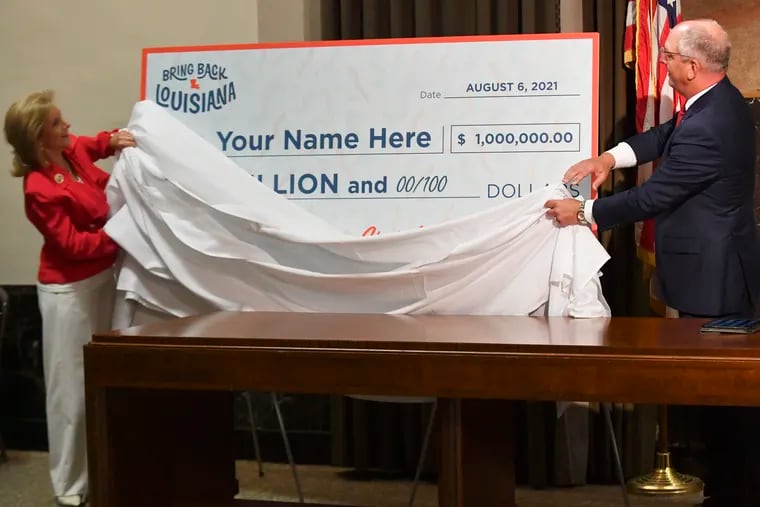 First lady Donna Edwards, left, and Gov. John Bel Edwards, right, unveil a giant check during a June news conference at the Louisiana State Capitol in Baton Rouge, La., to announce that Louisiana will participate in a lottery, giving cash prizes and scholarships to residents who have been vaccinated against the coronavirus.