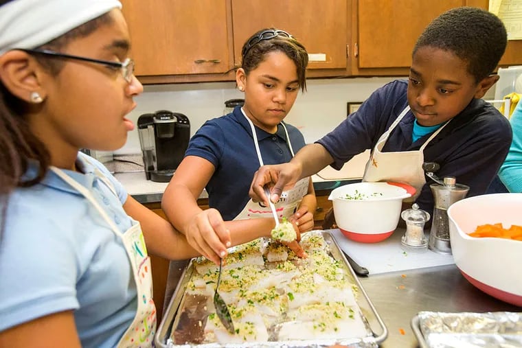 Fifth grade students (from left) Jatiana Cotto, Cristina Muriel, and Mahaaj Jones from Wiggins Prep in Camden sprinkle a bread crumb mixture on pieces of cod.