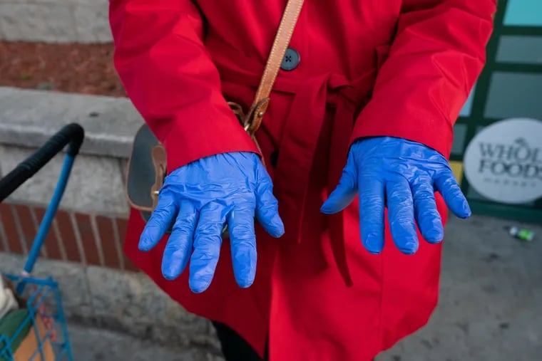A woman who does not mind her photograph being published, but who prefers not to have her name in the paper, shows the plastic gloves she is wearing while she grocery shops on South Street in Philadelphia, March 18, 2020.