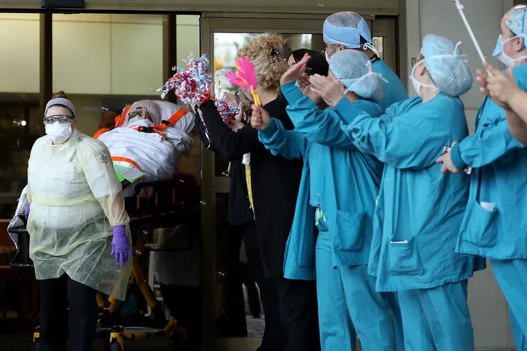 Medical workers cheer as recovering COVID-19 patient, Kim Dobson, 63, is discharged from Virtua Memorial Hospital in Mt. Holly, NJ on April 27, 2020. Dobson was transferred to a rehabilitation center to finish recovery before returning home.