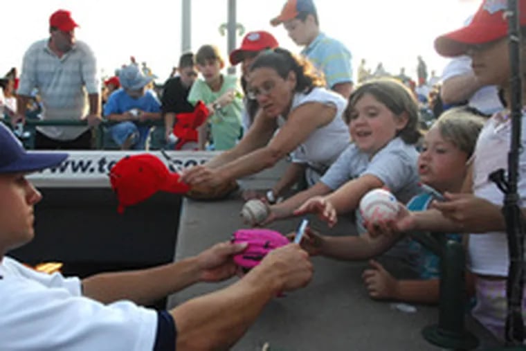 Young fans hold out their baseballs and gloves to get an autograph from a Cyclones player. Fans have taken the team to heart.