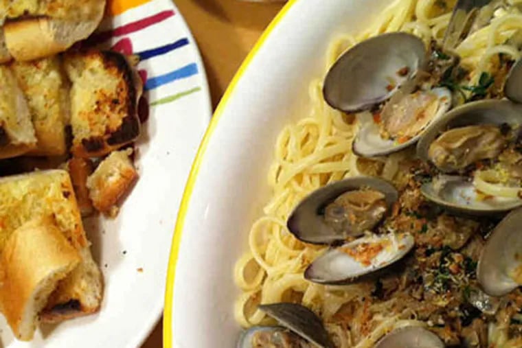 Finished clam pasta, with minced and whole shellfish, and a platter of garlic bread. (Craig LaBan / Staff)