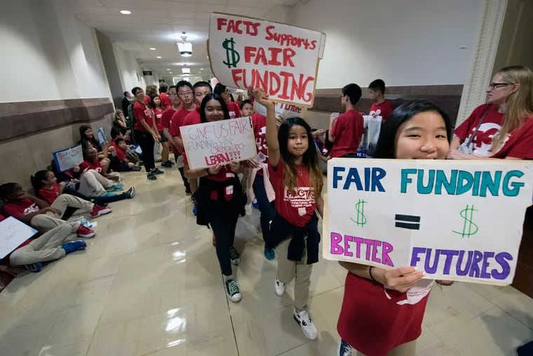 Students from the Folk Arts-Cultural Treasures Charter School in Philadelphia march with signs outside the state Supreme Court’s chamber in Philadelphia’s City Hall. Plaintiffs argue the state’s education-funding system is unfair.