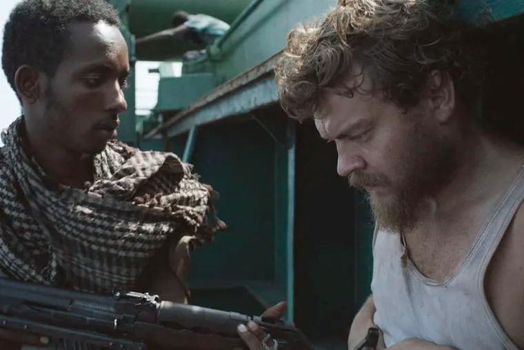 The hijacked ship's cook Mikkel, portrayed by Pilou Asb&#0230;k (right), interacts with a pirate, played by Abdi Rashid Yusuf.