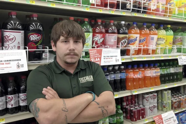 In this on Aug. 22, 2017 photo, Matt Gill, manager of Tischler Finer Foods in Brookfield, Ill., poses for a photo in the soda isle of the store. Gill says the Cook County tax on sweetened beverages reduced sales, because customers went elsewhere to buy soda and other drinks. The tax also could carry a political price for county board President Toni Preckwinkle and others who voted for it.
