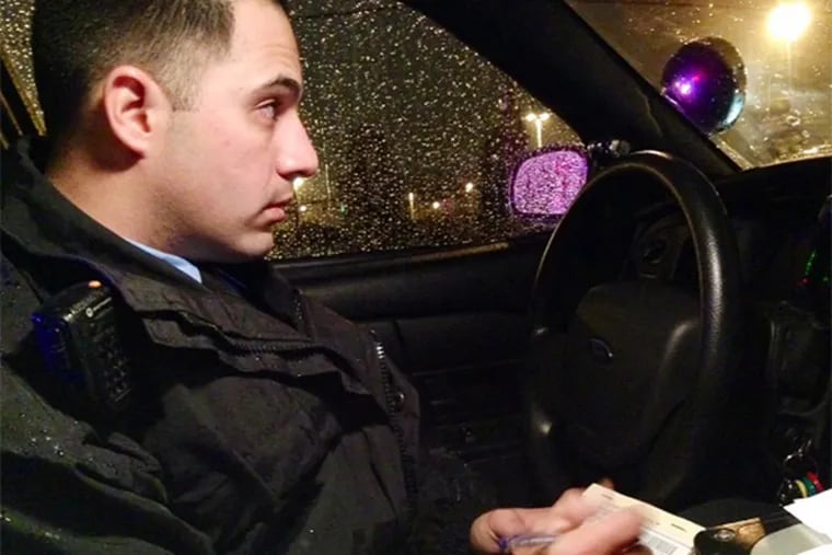 Officer Michael Levin keeps an eye out during a car stop as he writes a ticket for a man who made a brazen illegal U-turn on Wissahickon Avenue Tuesday night. (Morgan Zalot / Daily News Staff)