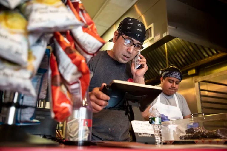 Owner Josh Kim answering the phone as Jorvan Ramos worked behind him at Spot Gourmet Burgers in Brewerytown on March 20, before Kim shut down to make repairs.