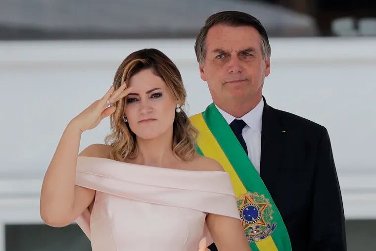 With her husband, Brazil's new President Jair Bolsonaro in the background, Brazil's new first lady Michelle Bolsonaro gives a military salute from the Planalto Presidential palace, in Brasilia, Brazil, Tuesday, Jan. 1, 2019. (AP Photo/Silvia Izquierdo)