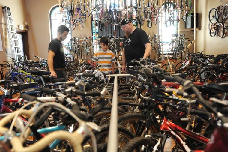 Pastor Scott Roth, right, assists 12 -year-old Paul Reichley, center, and his dad Zeke Reichley, left, select his new bike from the Bike and Sol shop in East Greenville.