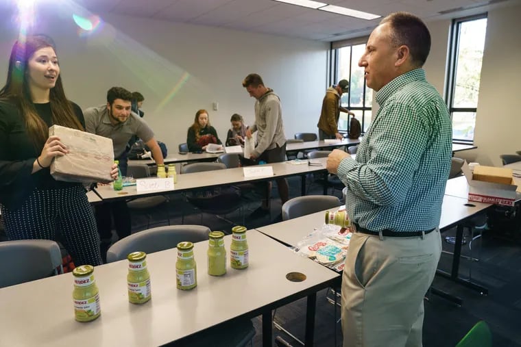 Professor George Latella after a retail class at St. Joseph's University, which offers undergraduate and graduate programs in food marketing. Latella has a several jars of Hormel foods displayed on the table as he talks with Maddy Trofa (far left) a customer executive at Hormel and an alumna of St. Joe's.