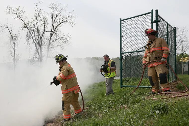 Wagontown Volunteer Fire Company engineer Sohn Stark, right, watches as firefighter Nick Sheplock, left, aims his hose at a small brush fire during a training exercise at the Chester County Public Safety Training Campus in Coatesville, Pa., on Saturday, May 5, 2018. Aardvark Video Works owner Mike Fanaro, center, films the exercise. Fanaro's company was hired by Communication Solutions Group, a public relations firm working with the Chester County Fire Chiefs Association, to produce television and movie theater commercials to help recruit volunteer firefighters.