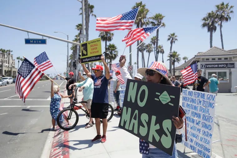 Demonstrators hold signs and U.S. flags as they protest the lockdown and wearing masks on Saturday in Huntington Beach, Calif.