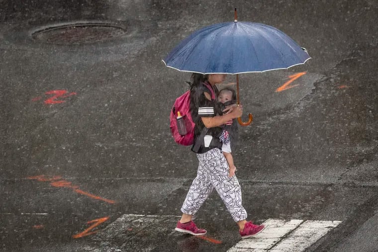 A young woman walks with a baby underneath her umbrella during a heavy rain in Center City on Monday.