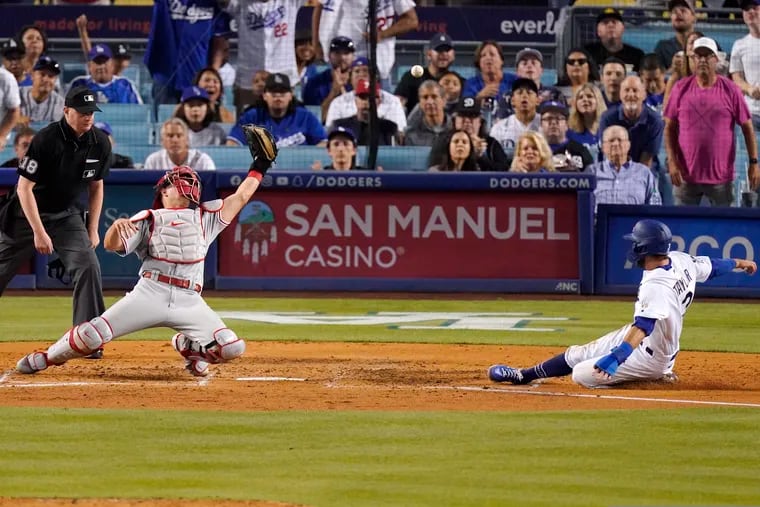 The Dodgers' Chris Taylor (right) scores on a single by Zach McKinstry as Phillies catcher J.T. Realmuto misses the ball on Tuesday.