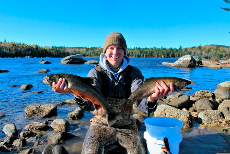 In this Oct. 26, 2018 photo, University of Maine graduate student Brad Erdman holds an Artic charr, left, and a brook trout, right, at Floods Pond near Otis, Maine. Scientists in Maine are in the middle of a project to use DNA to help preserve Arctic charr, which are at the southern end of their range in the state.