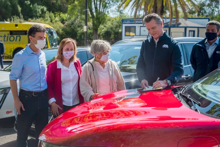 On the hood of an electric car, California Gov. Gavin Newsom signs an executive order requiring all new passenger vehicles sold in the state to be zero-emission by 2035 after a press conference on Wednesday.