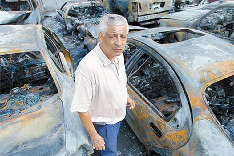 J & Sons owner Jose LaTorre Sr. stands next to cars that were set afire at his lot. (David Maialetti / Staff Photographer)