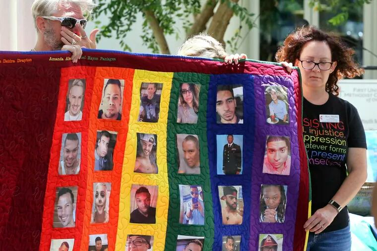Douglas Barrett, left, and Rev. Shelly Denmark, with others, hold a memorial quilt during the tolling of the bells and reading of the names at First United Methodist Church in Orlando, Fla., Wednesday, June 12, 2019, on the 3rd anniversary of the Pulse nightclub massacre. (Joe Burbank/Orlando Sentinel via AP)