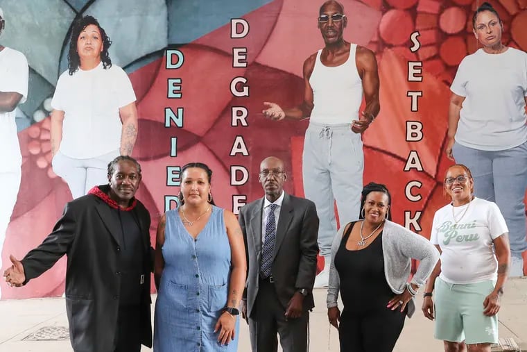 From left, Jondhi Harrell, Naiymah Sanchez, John Thompson, Michelle Simmons, and Faith Bartley in front of a mural of themselves and others (not pictured) at the underpass on 21st and JFK in Philadelphia. The mural highlights formerly incarcerated individuals who have reentered society and have since made an impact in the city of Philadelphia.