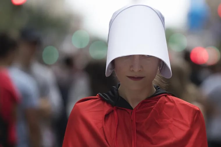 A unidentified woman protests at Broad Street for the pending arrival of Vice President Mike Pence at the Union League, in Philadelphia, Monday, July 23, 2018. Dozens of demonstrators dressed as characters from the novel-turned-TV series "The Handmaid's Tale" descended on downtown Philadelphia to protest Pence's visit. (Jose F. Moreno /The Philadelphia Inquirer via AP)