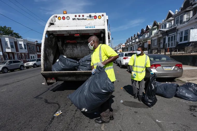 Sanitation workers Lawrence Brown, left, and Rashan Purcell, right, collect trash on East Allegheny Ave., in Philadelphia July 27, 2020.