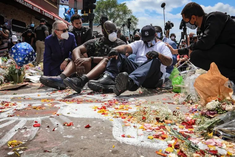 An emotional Terrence Floyd, second from right, is comforted as he sits at the spot at the intersection of 38th Street and Chicago Avenue, Minneapolis, Minn., where his brother George Floyd, encountered police and died while in their custody.