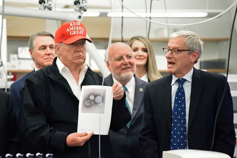 President Donald Trump holds a photograph of coronavirus as Dr. Steve Monroe,right, with CDC speaks to members of the press at the headquarters of the Centers for Disease Control and Prevention in Atlanta on Friday.
