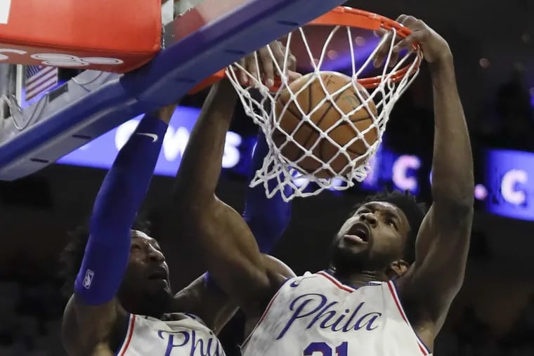 Sixers center Joel Embiid dunks the basketball past teammate forward Robert Covington during the first-quarter against the New Orleans Pelicans on Friday, February 9, 2018 in Philadelphia.