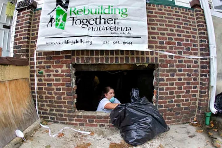 Volunteer Adelina Saturno deposits a bag of trash outside a basement window of a house on Chancellor Street in West Philadelphia, where crews spent the day at work.