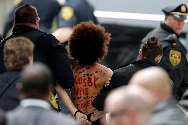 A protester is led away after jumping in front of actor Bill Cosby as he arrives for the beginning of his sexual assault retrial at the Montgomery County Courthouse in  Norristown, PA on April 9, 2018.