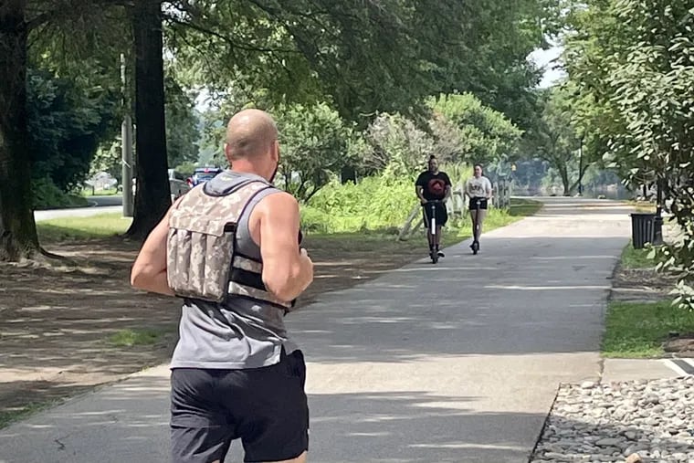 A runner and scooter riders utilize the walkway along Kelly Drive Sunday morning, not far from the parking lot where police early Saturday found the body of a man who had been fatally shot in the head.