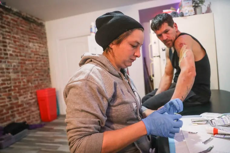Jen Shinefeld, a Field Epidemiologist, cleans the wound on the arm of Nick Gallagher at Savage Sisters, an outreach organization based in Kensington, in Philadelphia on Tuesday, Jan. 10, 2023. The staff at Savage Sisters help treat xylazine wounds and help people through withdrawal.
