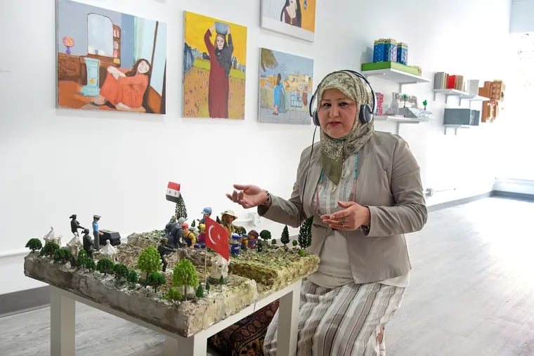 Fadaa Ali kneels in front of a sculpture she created of Syrian refugees escaping to Turkey as part of the "Friends, Peace, and Sanctuary" exhibit at Twelve Gates Arts.