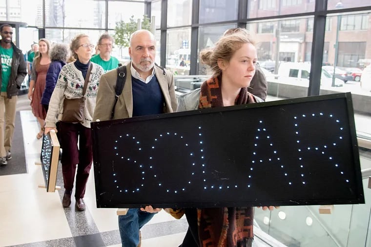 Molly Copeland carries a “solar” sign into Peco headquarters. Activists have demonstrated there every few weeks — the first time Peco has been targeted by protesters in decades.