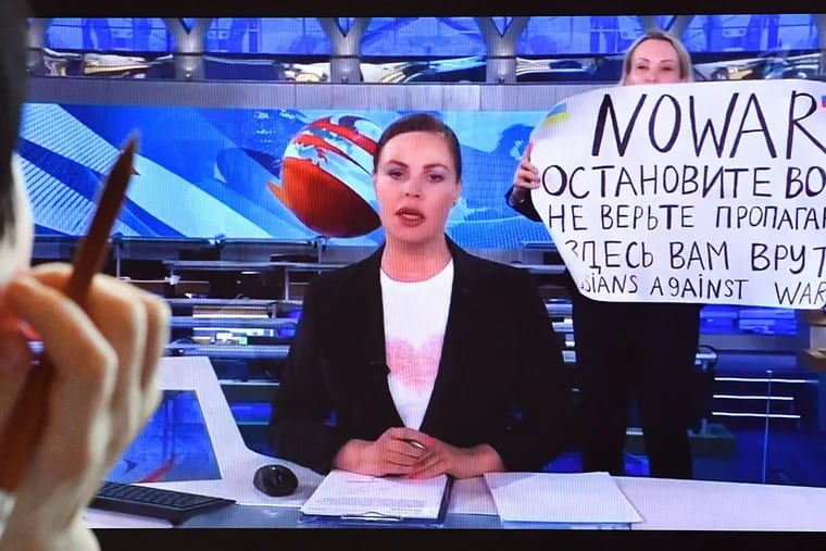 As news anchor Yekaterina Andreyeva, center, discusses Russia's relations with Belarus, Marina Ovsyannikova, right, burst into view, holding up a handwritten poster saying "No war" in English.